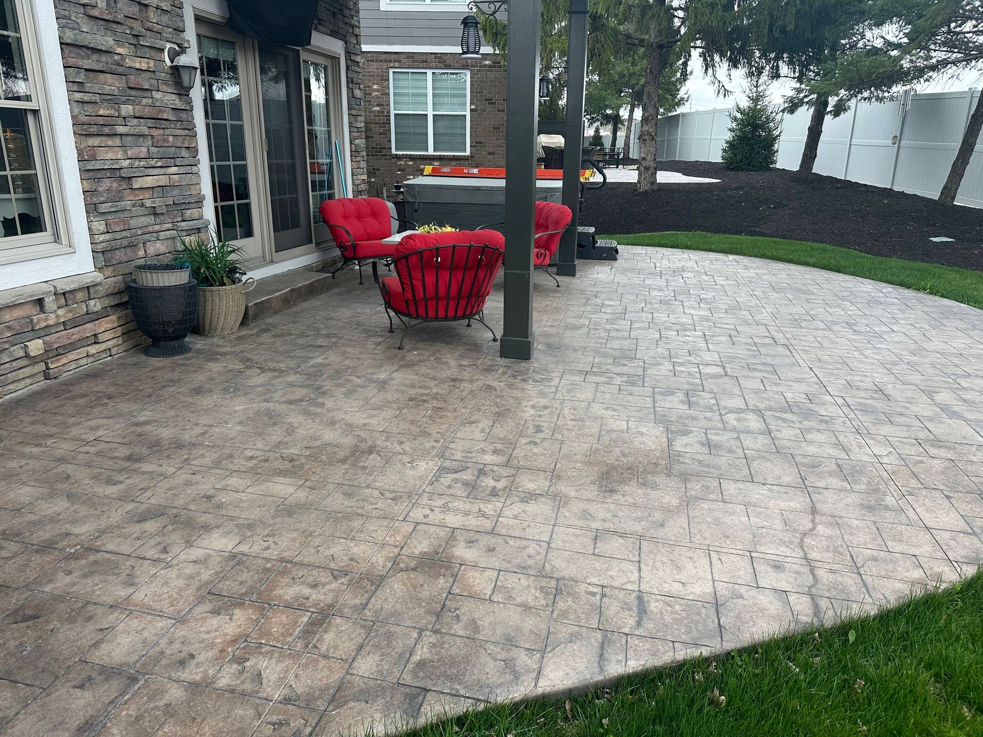 Stamped concrete patio with red outdoor chairs beside a brick house and lawn