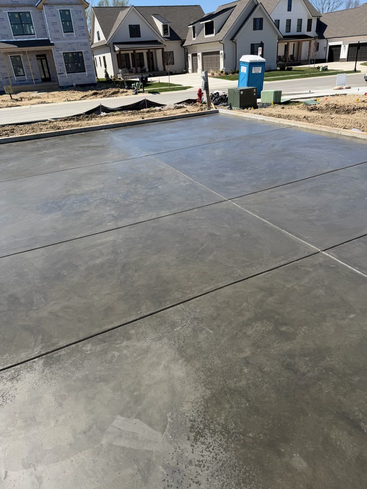 Freshly poured concrete driveway in front of new suburban houses, with a blue portable toilet nearby.