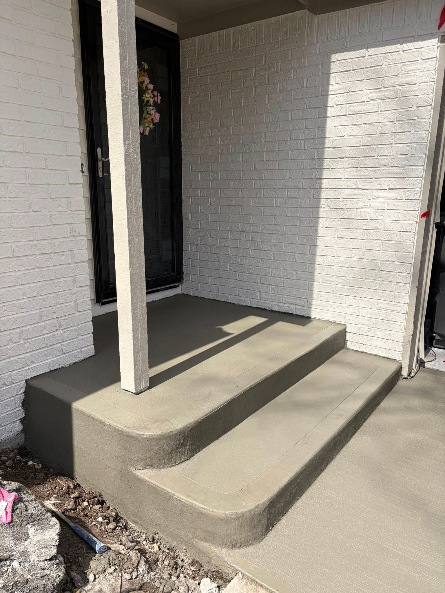 Front porch with two rounded concrete steps, white brick walls, and a black front door.