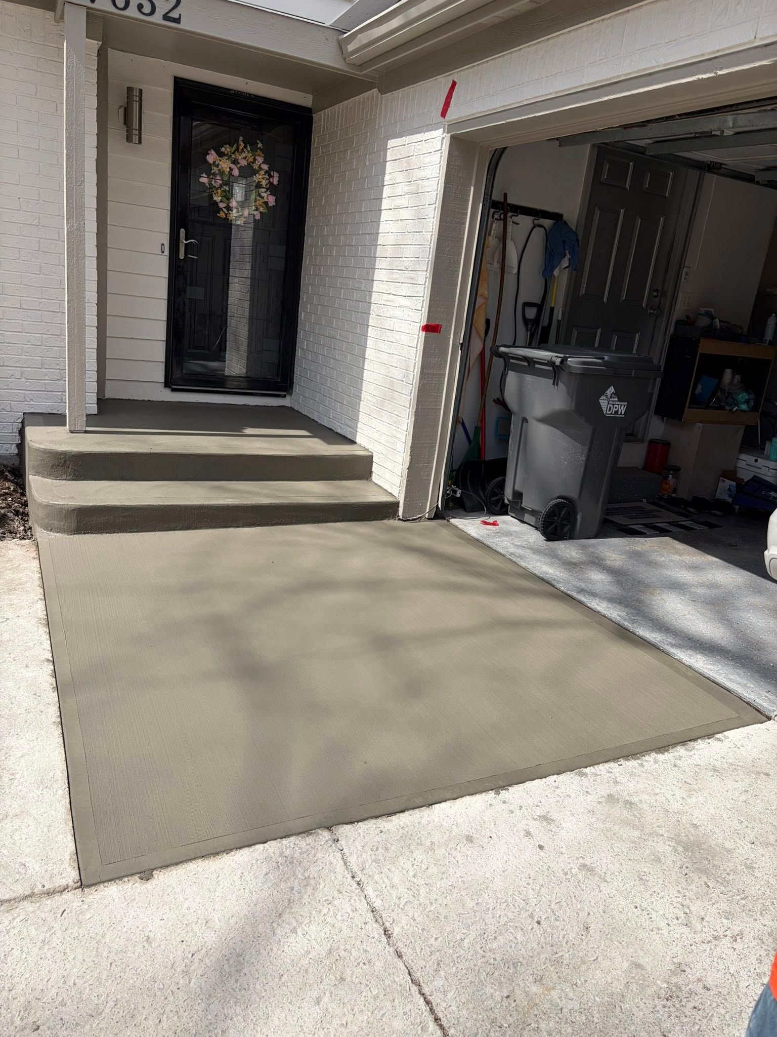 Front entrance with concrete steps, a black door, and a garage opening beside a fresh concrete driveway.