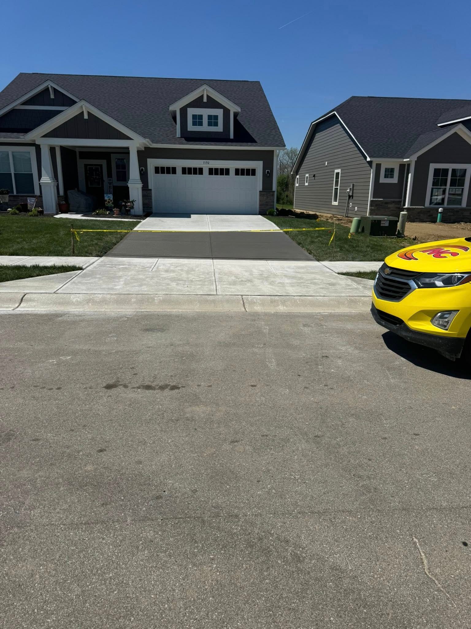 Suburban house with driveway and parked yellow car at the curb under a clear sky