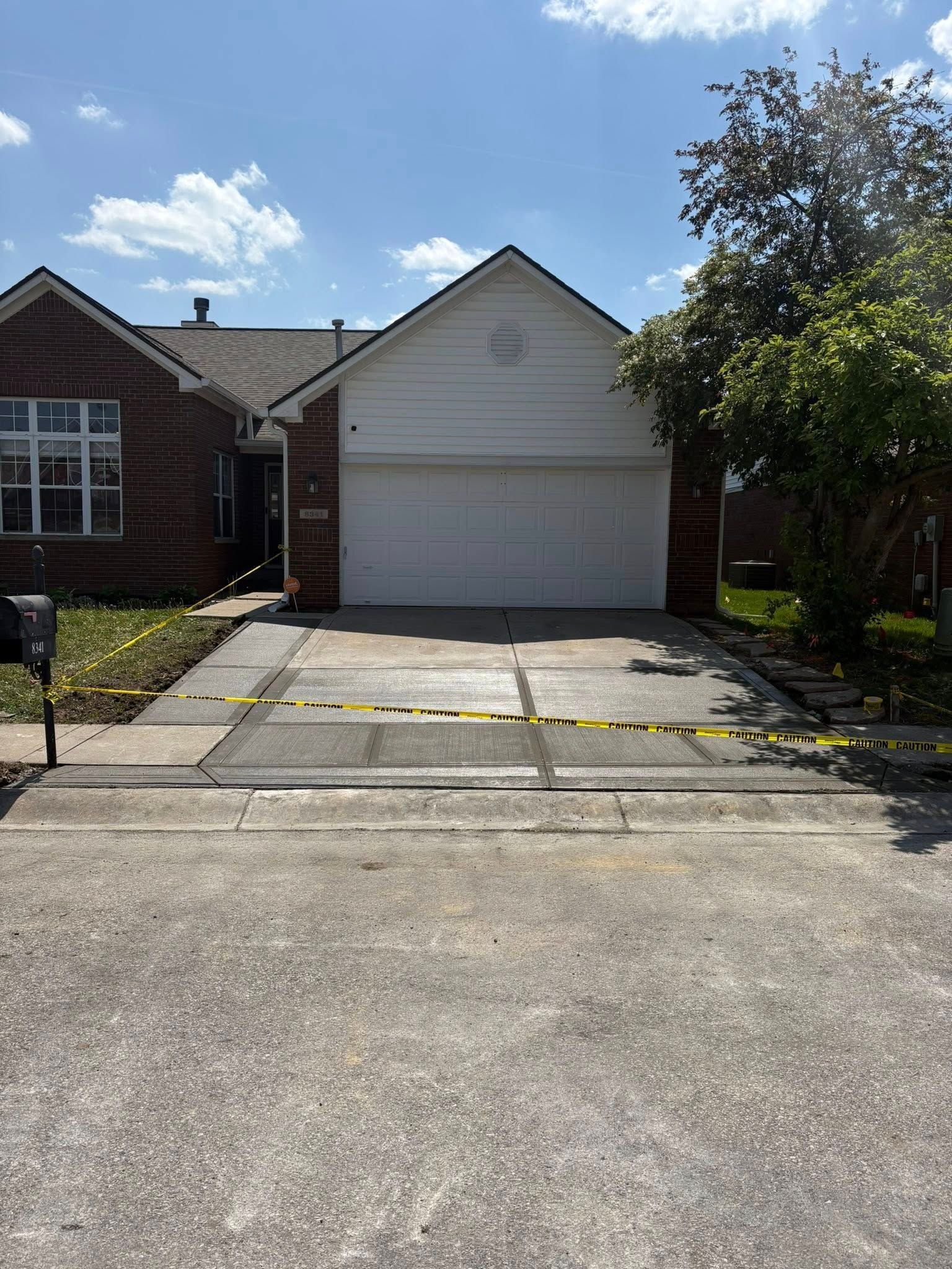 Suburban house with white garage door and driveway under bright sun, trees and lawn on both sides