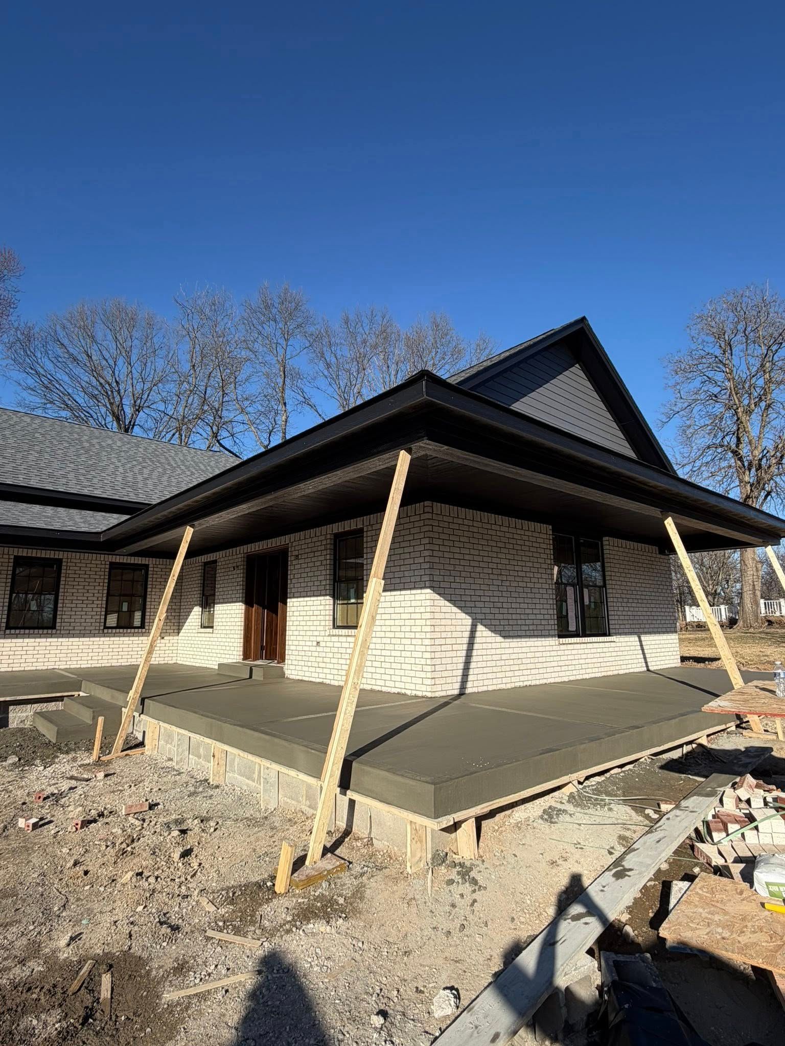 House under construction with porch posts and dark roof under a clear blue sky