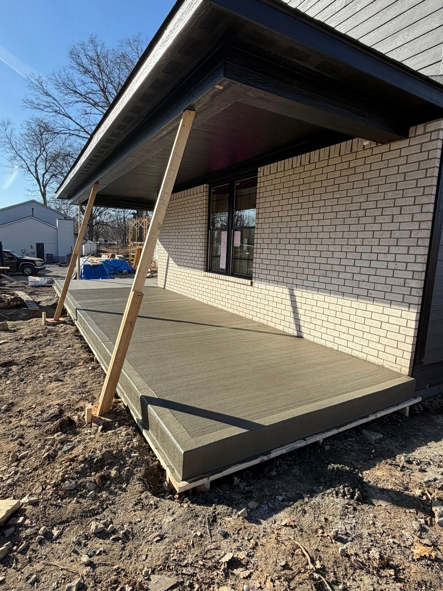 Front porch ramp under construction beside a brick house, with wooden supports and poured concrete.