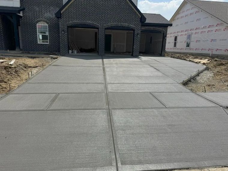 Concrete driveway leading to a stone house under construction, with unfinished landscaping on both sides