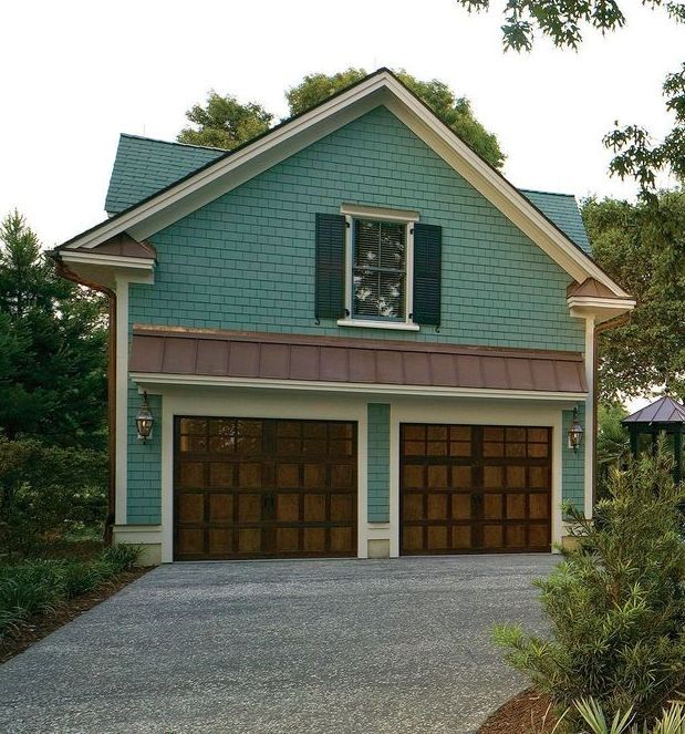 Teal two-car garage with a steep gabled roof and driveway, framed by trees and shrubs