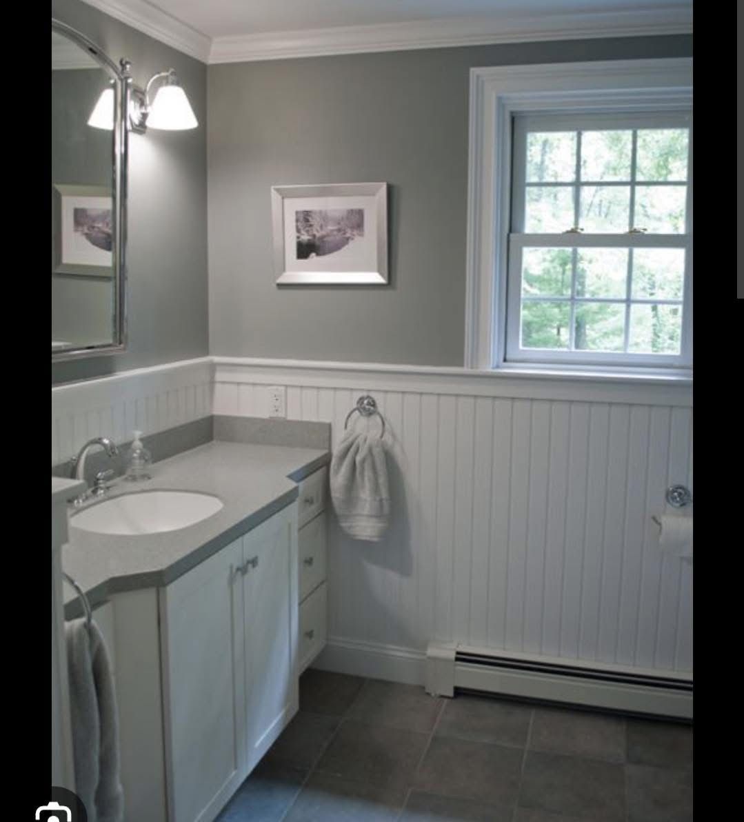 Bathroom with gray walls, white wainscoting, a vanity with a white cabinet and gray countertop, and a window.