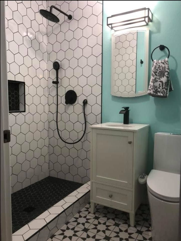 A small bathroom featuring a walk-in shower with black-and-white hexagon tiles, a teal wall, vanity, and white toilet.