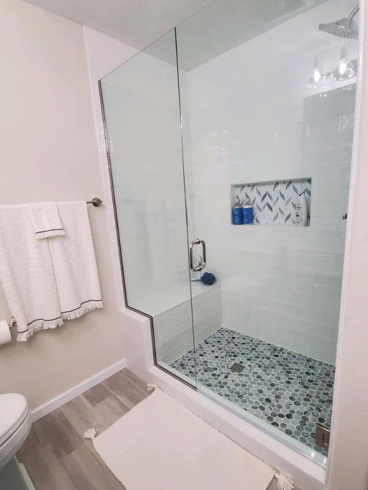 A modern bathroom with a glass-enclosed shower featuring pebble tile flooring, a tiled wall niche, and a white towel.