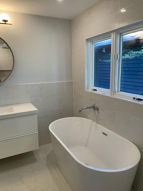 A modern bathroom featuring a white freestanding bathtub, a wall-mounted faucet, a vanity, and a round wall mirror.