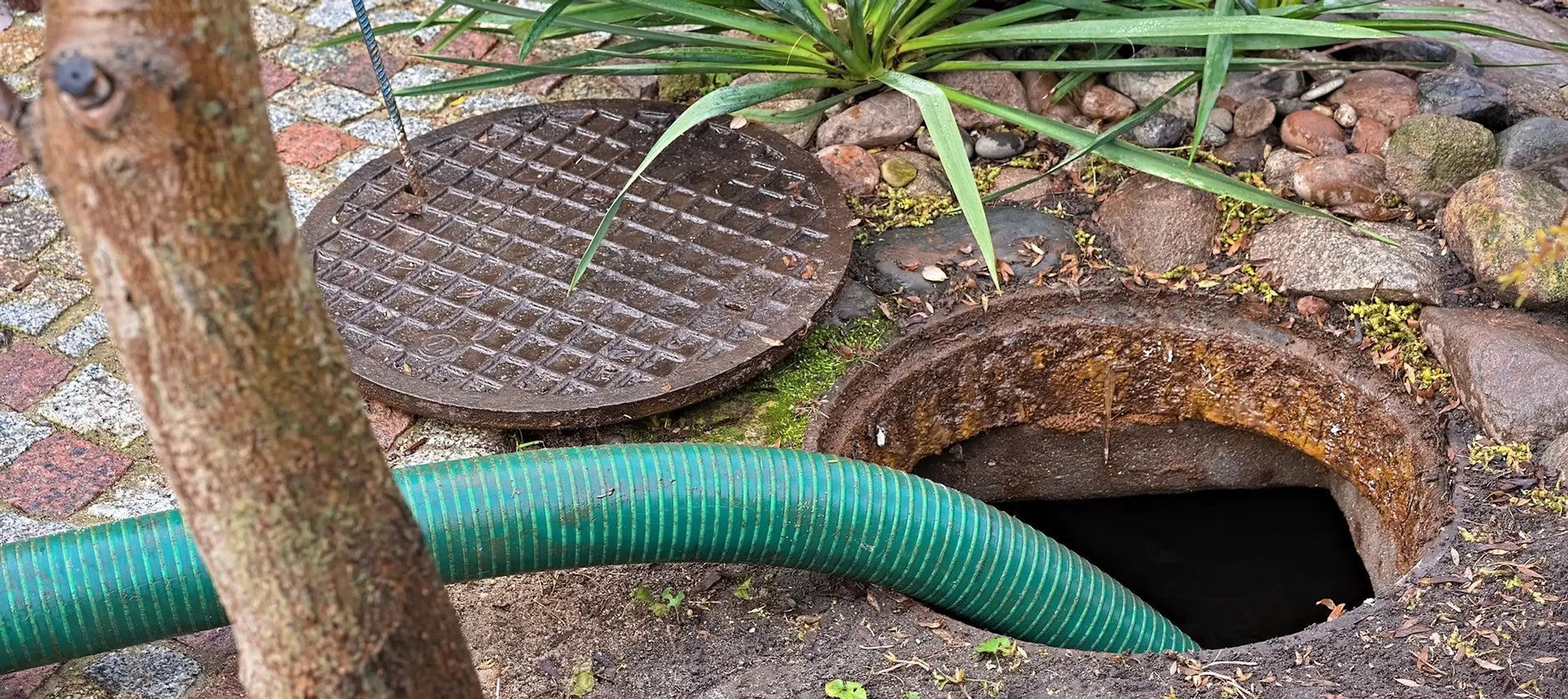 Green drainage pipe connected to a sewer opening with a cover grate.