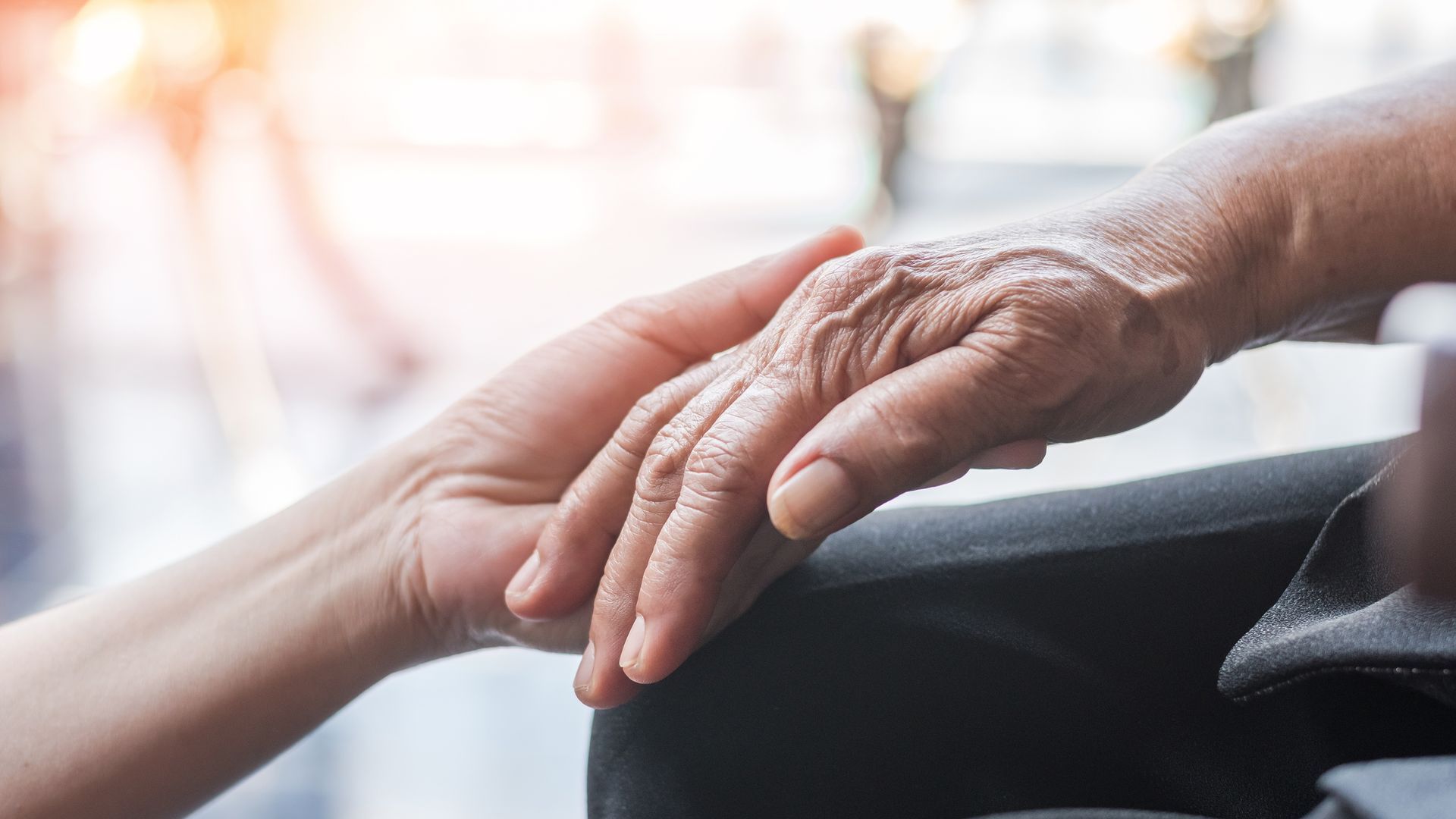 A hand gently holding the wrinkled hand of another person, showing comfort and care.
