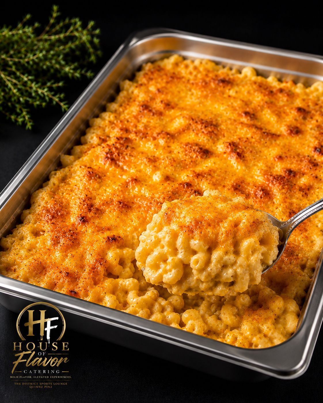 Baked macaroni and cheese in a metal tray, golden-brown on top with a serving spoon.