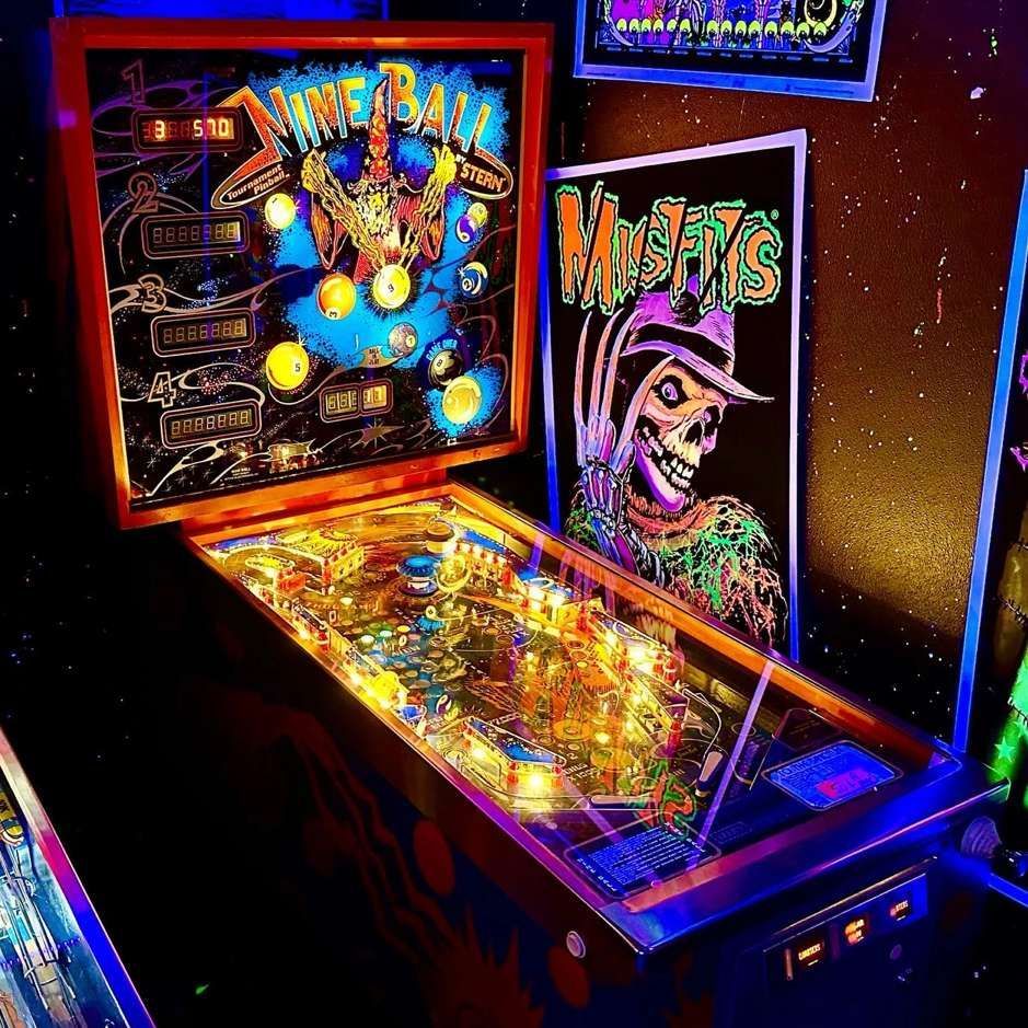 Neon-lit pinball machine with colorful arcade artwork in a dark room