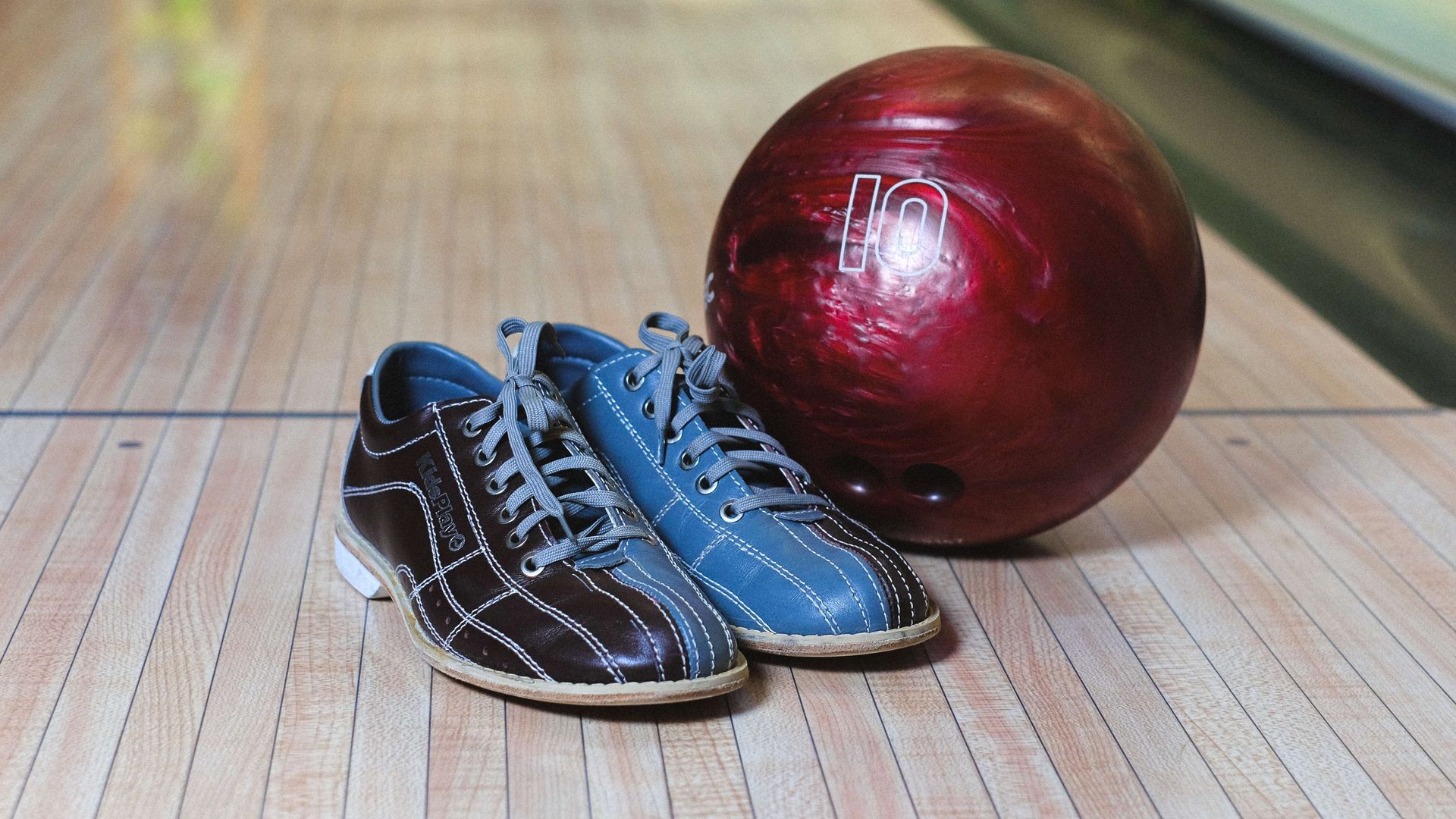 Blue and black bowling shoes beside a red bowling ball on a wooden lane