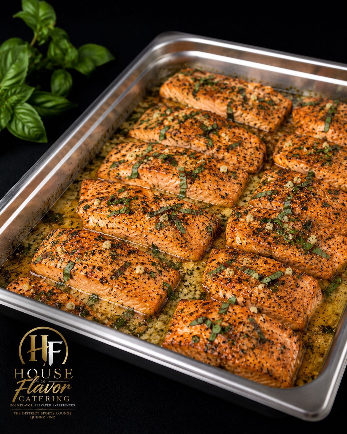 Baked salmon fillets in a metal tray, topped with herbs and seasoning