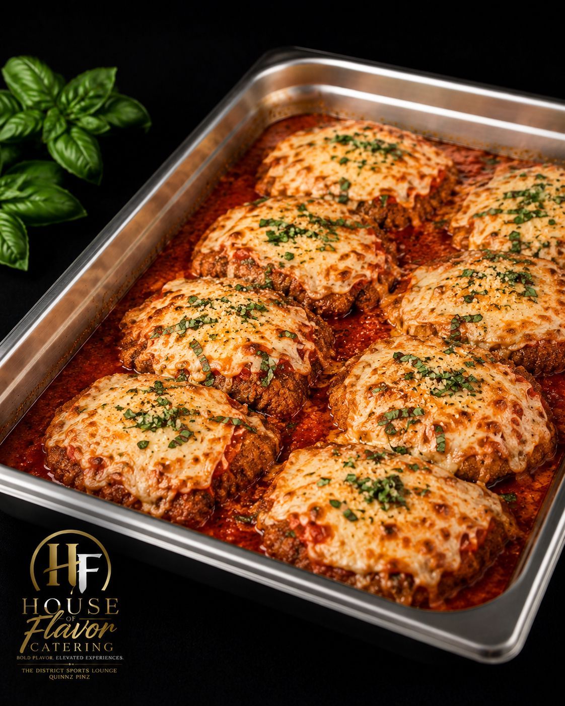 Baked cheesy chicken in a metal tray, topped with herbs and red sauce.