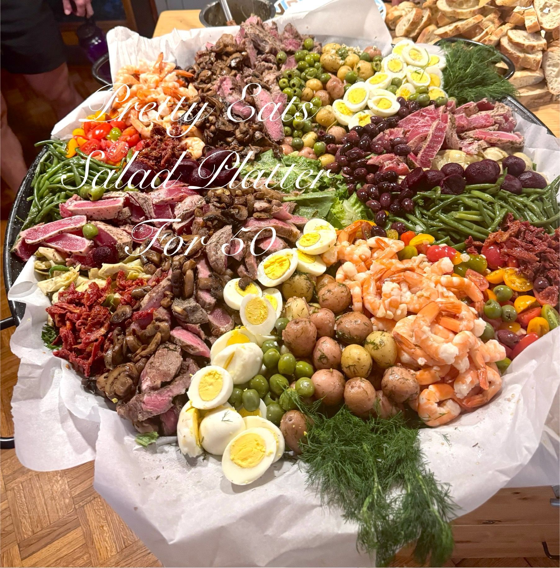 Large salad platter with meats, hard-boiled eggs, shrimp, vegetables, and herbs on a table
