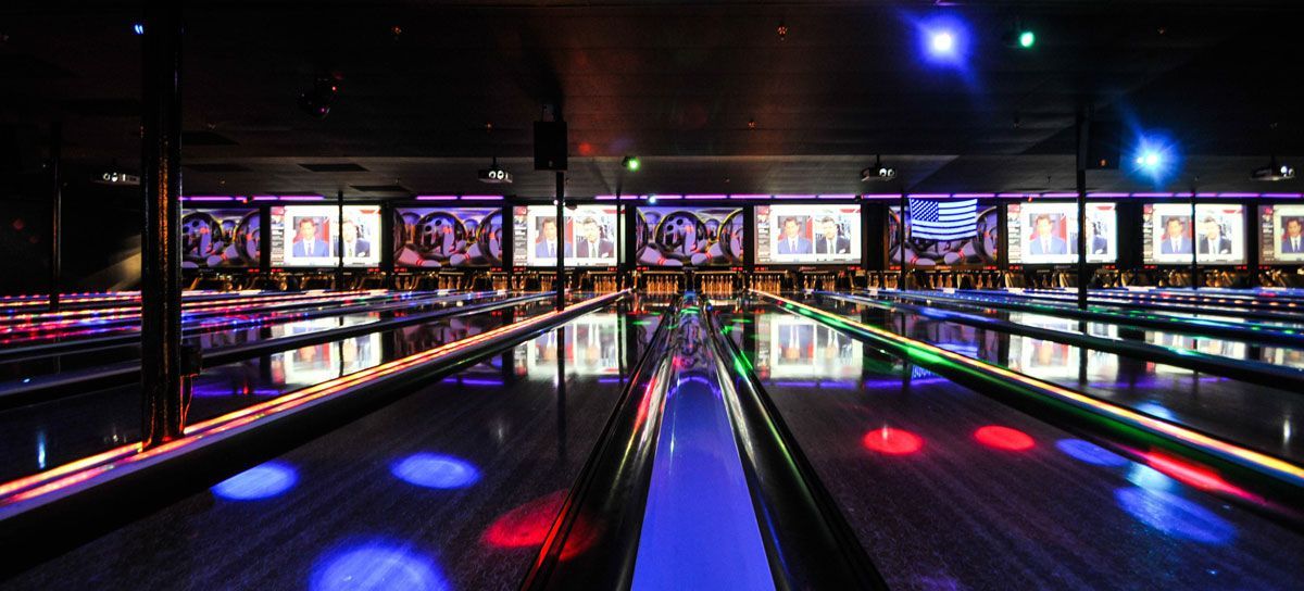 Bright neon-lit bowling alley with colorful lane lights and score screens in the distance