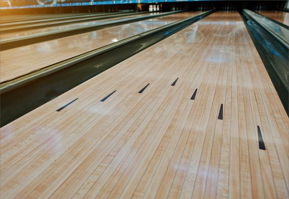 Empty bowling lanes with polished wooden boards and black lane markers, viewed from a low angle