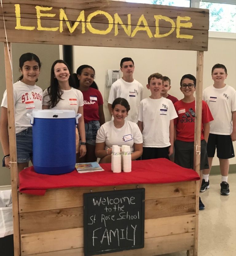 The Image shows several students behind a table with a sign that says Lemonade overhead. The bottom of the table has a sign that says