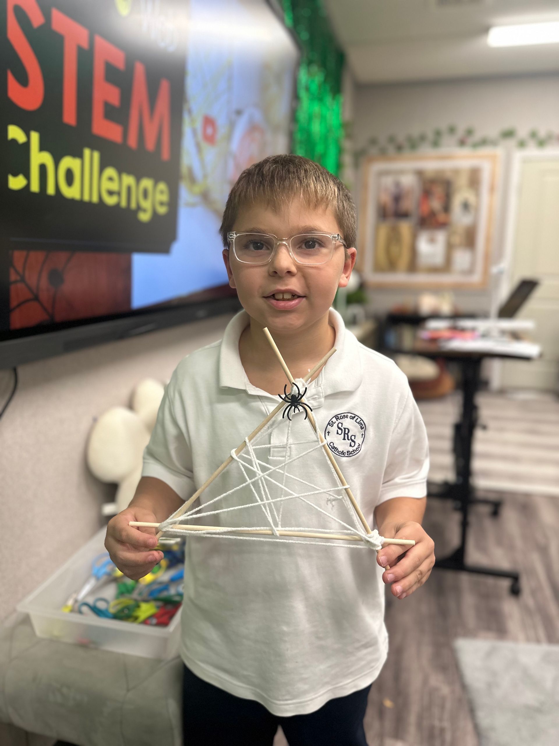 Student holds a triangle of skewers held together by a white rope to imitate a spider web