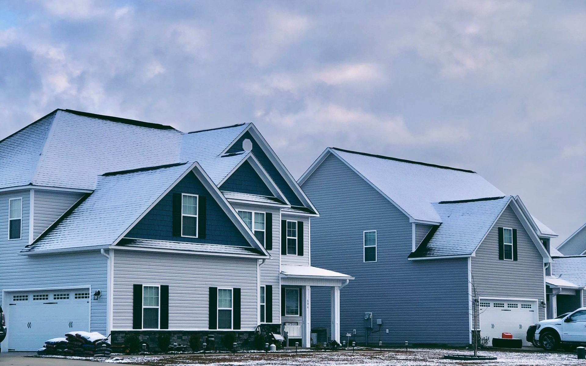 A row of houses with snow on the roofs and cars parked in front of them.