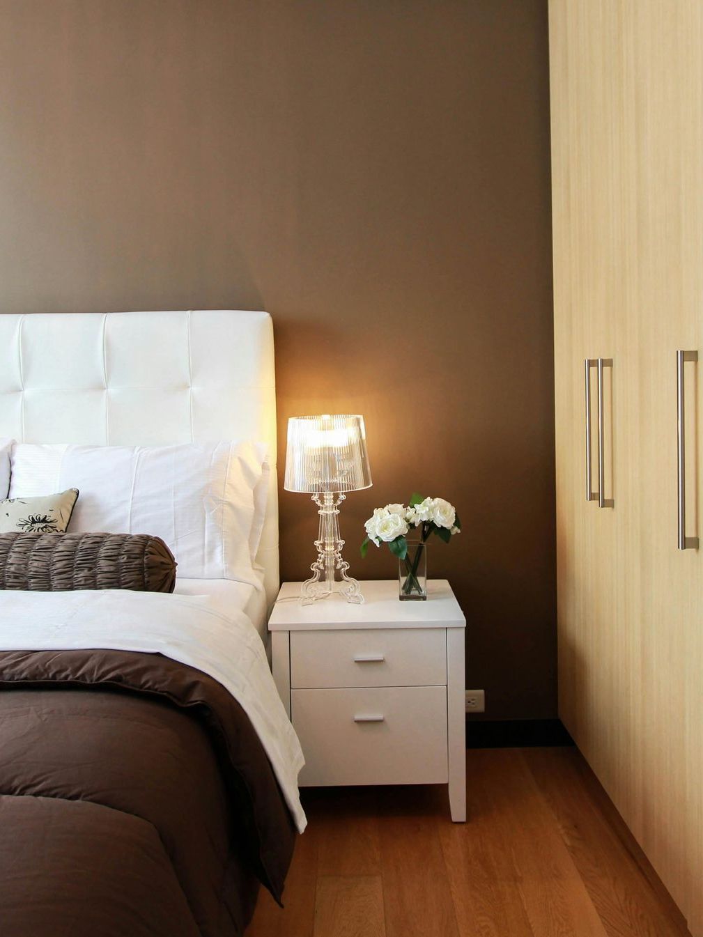 Bedroom with white bed, brown blanket, white nightstand, and brown wall.