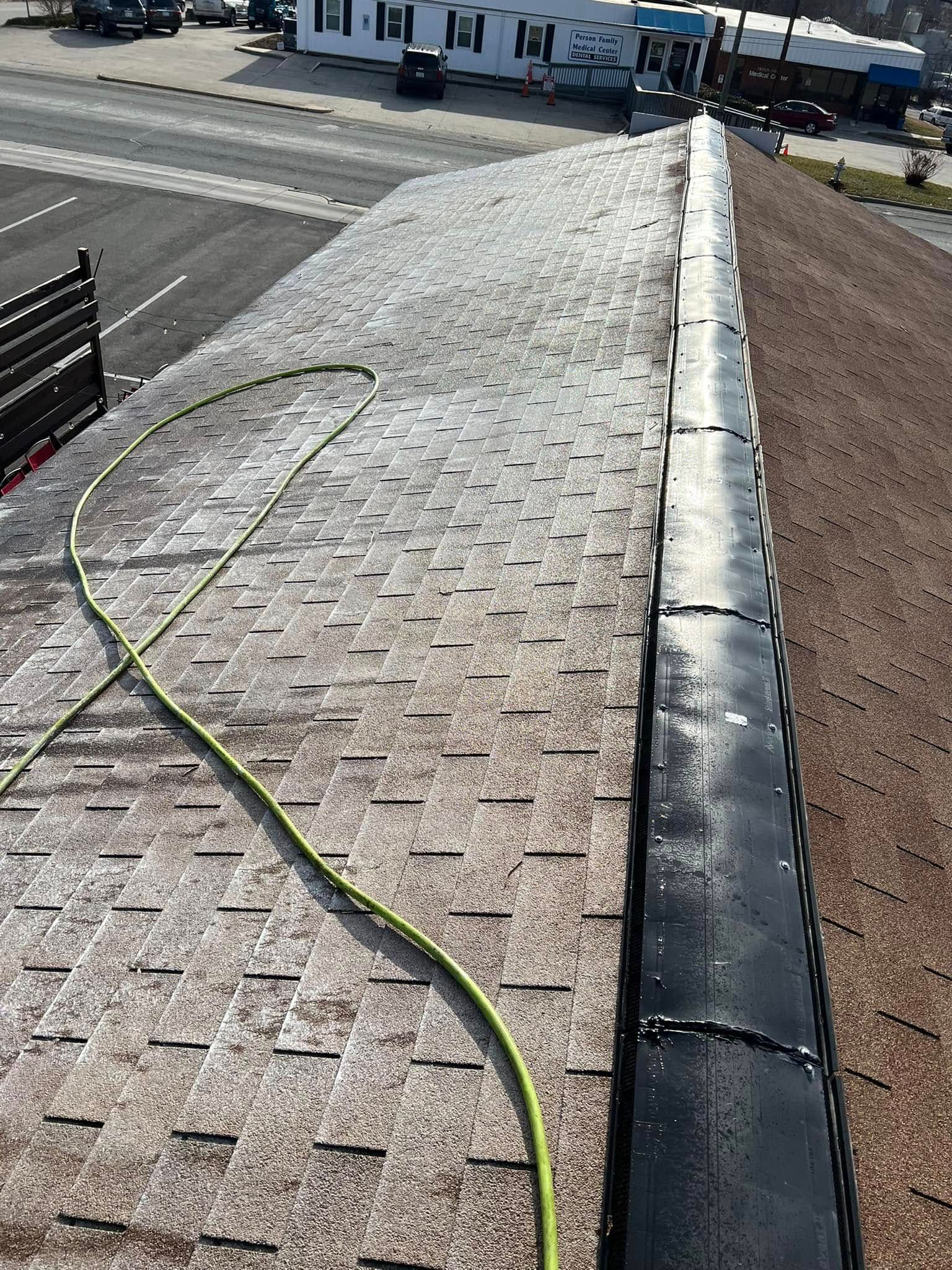 Roof edge with a green hose draped across shingles beside a curb and street