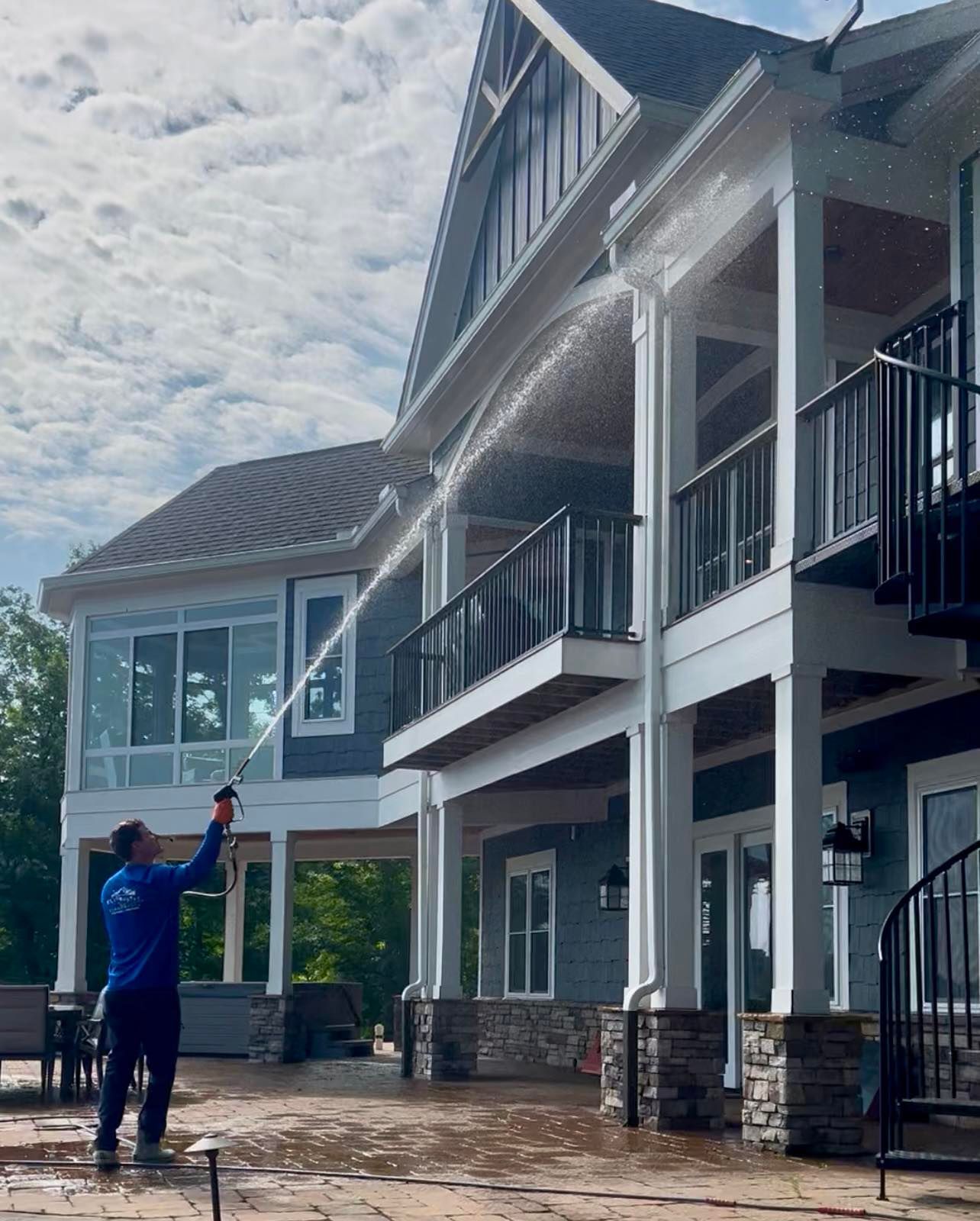 Person in blue points toward a two-story house with white siding and balconies.