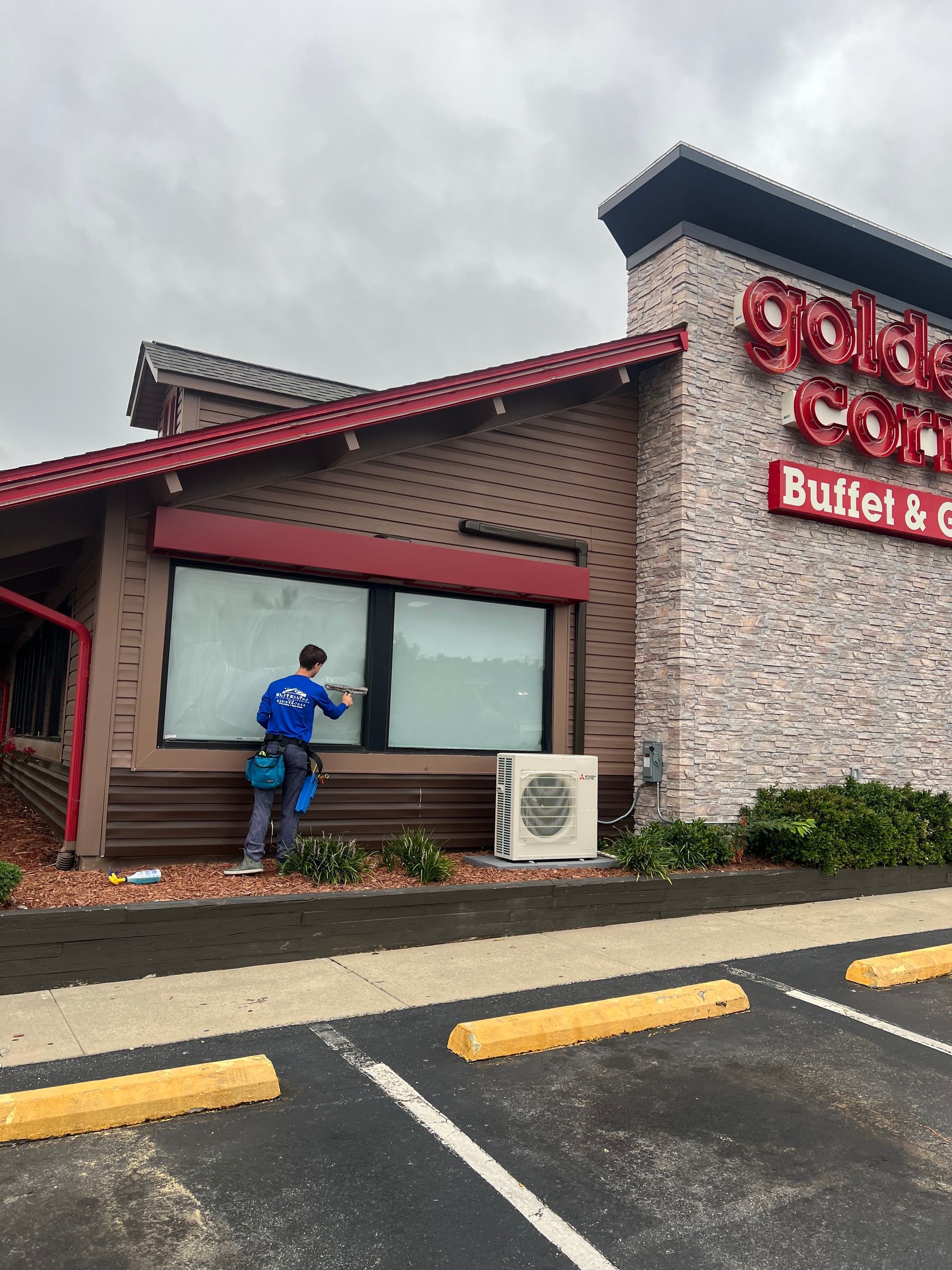 Person in blue jacket standing outside a restaurant, reaching toward a window under a red roof.
