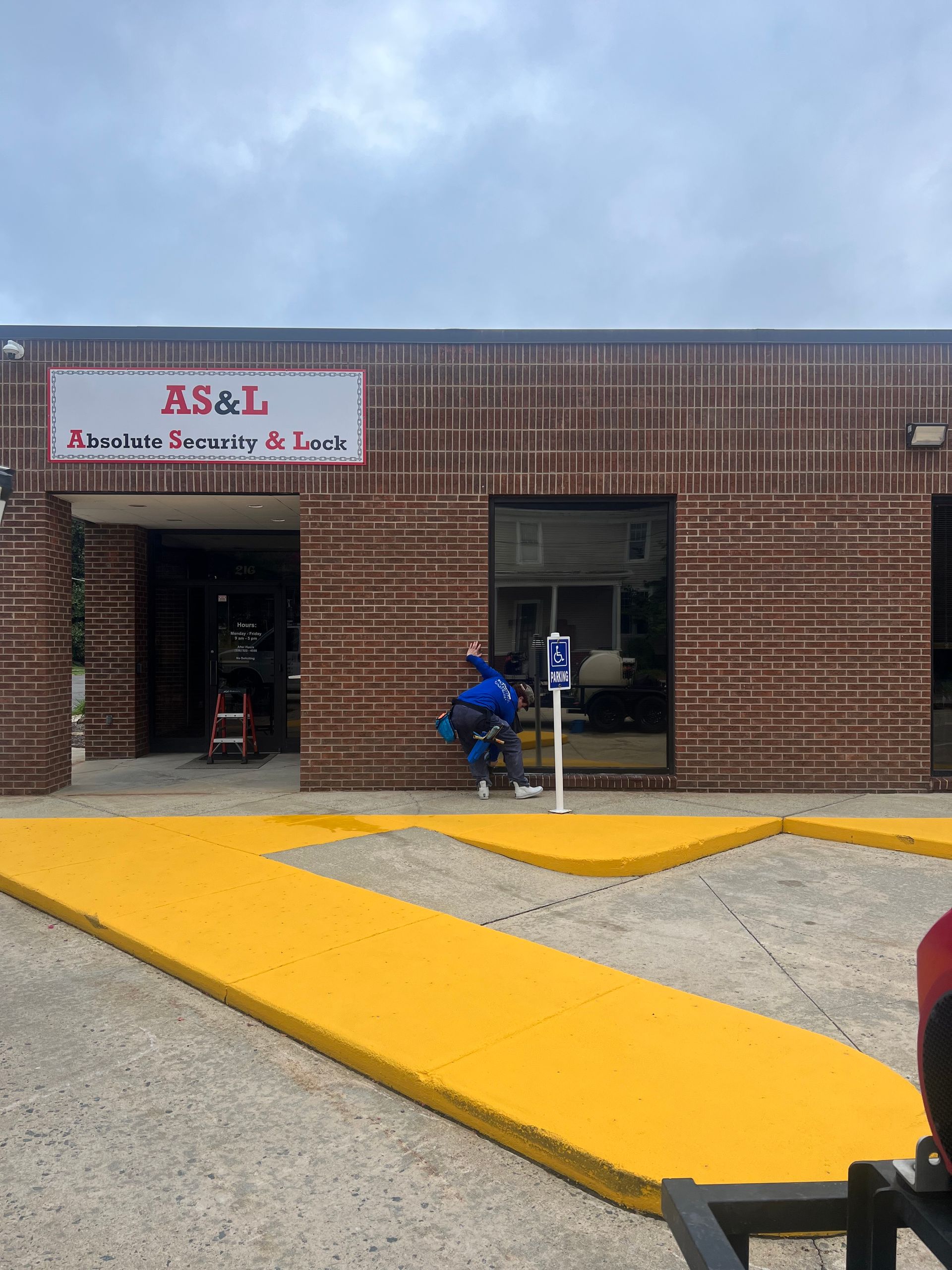 A person cleans windows of a storefront. They wear a blue shirt, stand outside, and use a squeegee.