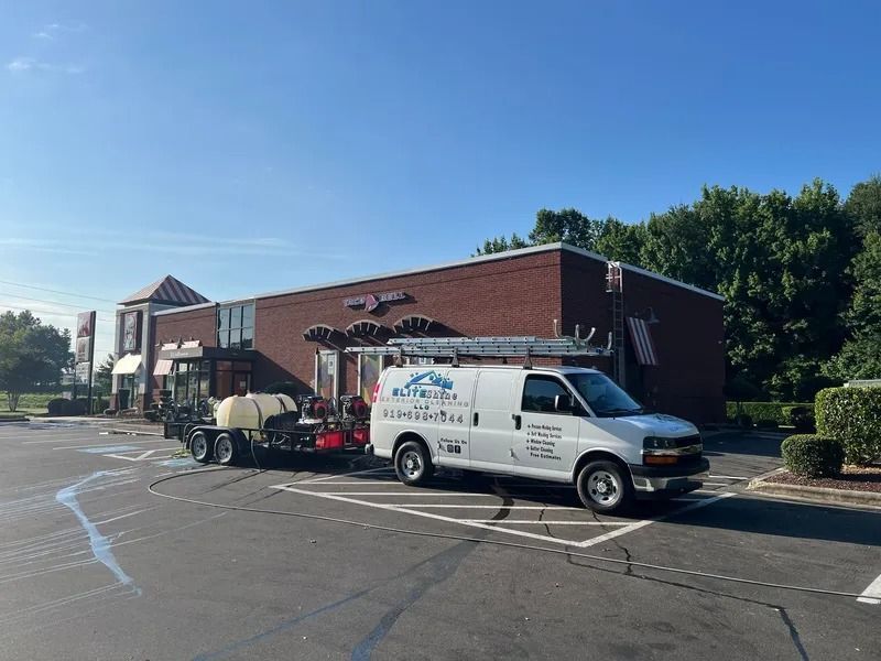 White van with trailer parked in front of a brick building on a sunny day.