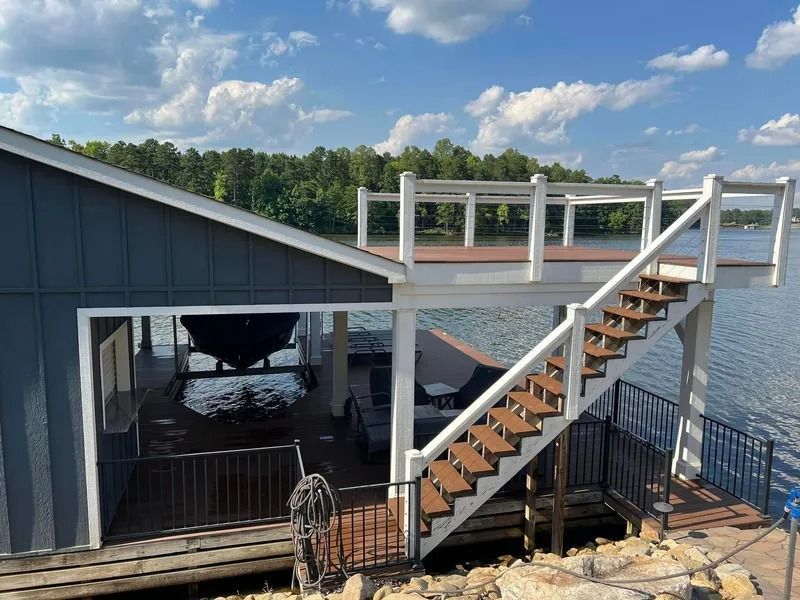 Dock house with stairs, white railings, and a boat slip on a lake. Blue siding, brown deck.