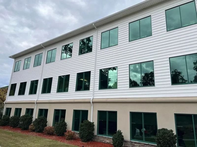 Two-story building with white siding, tinted green windows, and a tan base, under a cloudy sky.