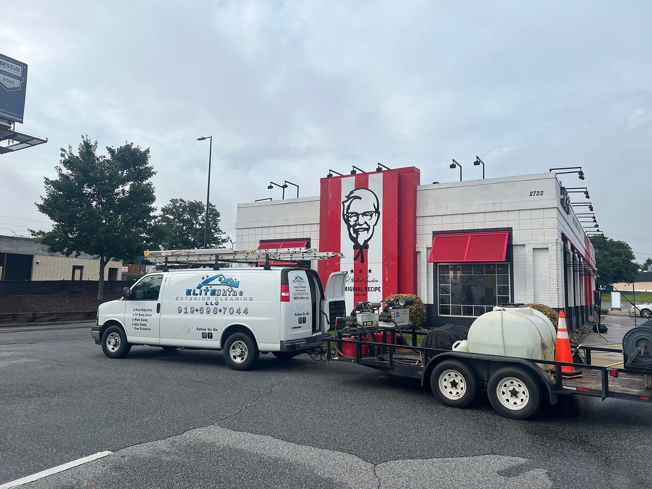 White van and trailer parked outside a KFC restaurant. Maintenance work is underway; the building is white with red accents.