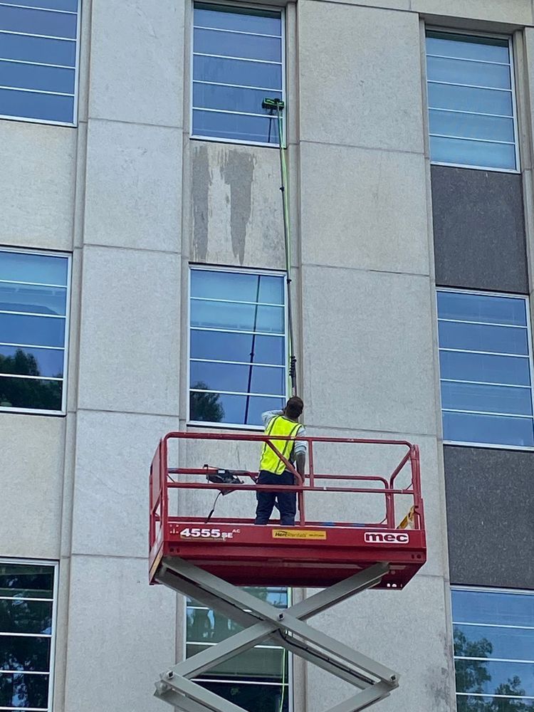 Person on a red lift washes a tall building's windows with an extended pole brush.