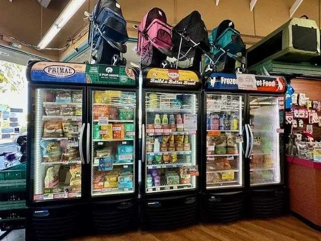 Three refrigerated displays in a pet store, stocked with various pet food and treats.