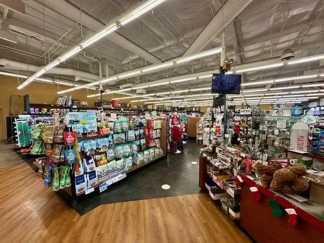 Interior of a pet supply store with shelves of products, wooden floors, and overhead lights.