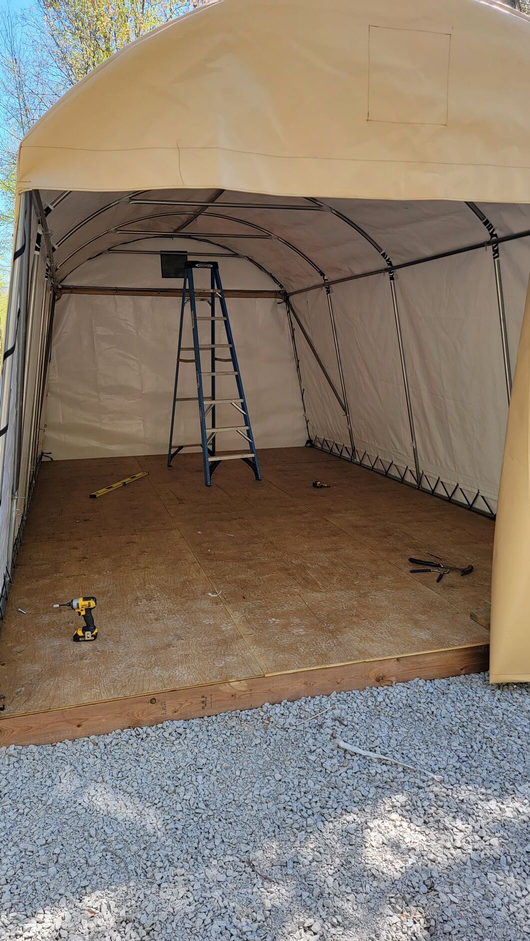 Interior view of a tan tarp shelter with a wooden floor, ladder, and tools.