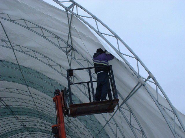 Person on a lift working on a white and green structure. Outdoors on a cloudy day. Cover-Tech Replacement Covers.