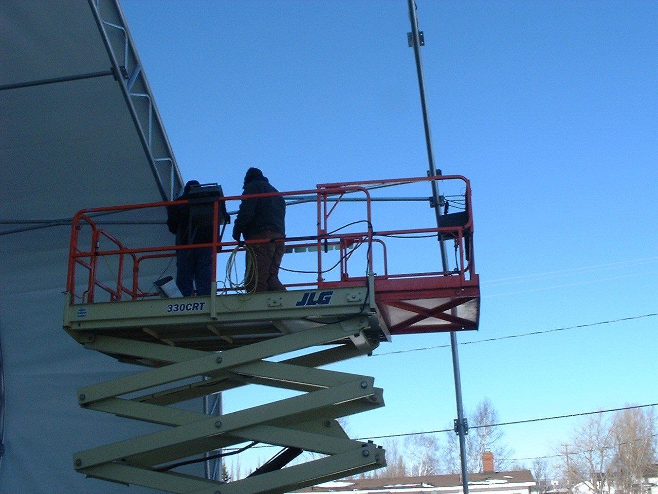 Two workers on a scissor lift, attaching something to a cable against a blue sky. Cover-Tech Replacement Covers.