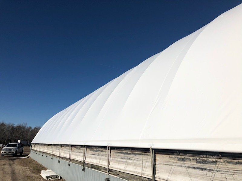 White arched roof structure against a clear blue sky, with a truck parked nearby. Cover-Tech Replacement Covers.