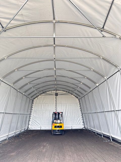 Forklift inside a white arched shelter. The ground is dark, and the structure is metal.