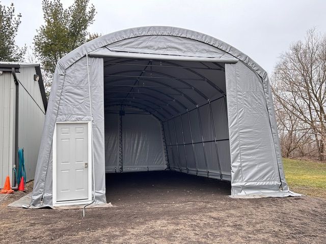 A large gray arched-roof storage structure with a door on the side and a wide open entrance.