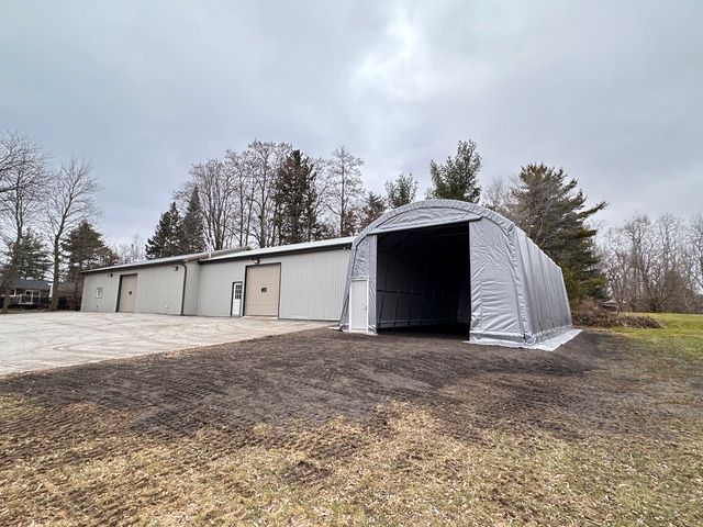 A large, gray arched storage building sits next to a metal building with several bays on a cloudy day.