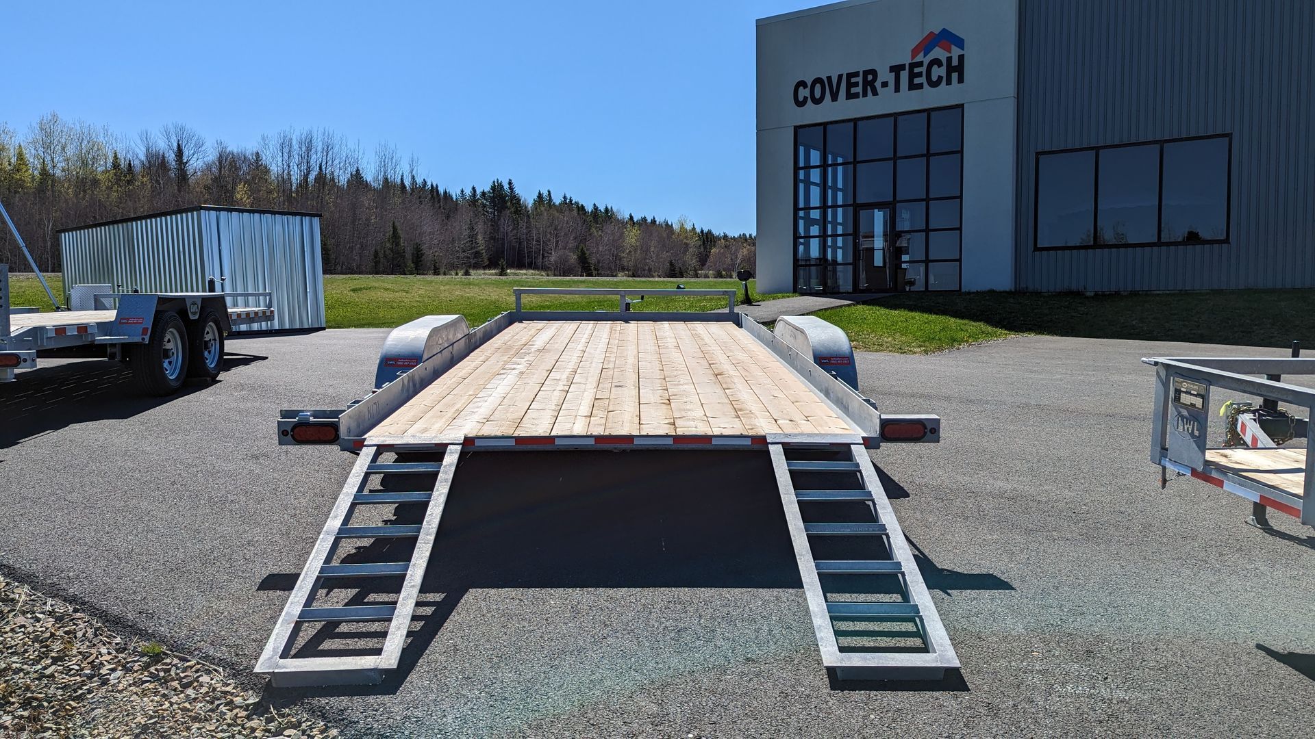 A trailer with ramps is parked in front of a building that says cover tech.