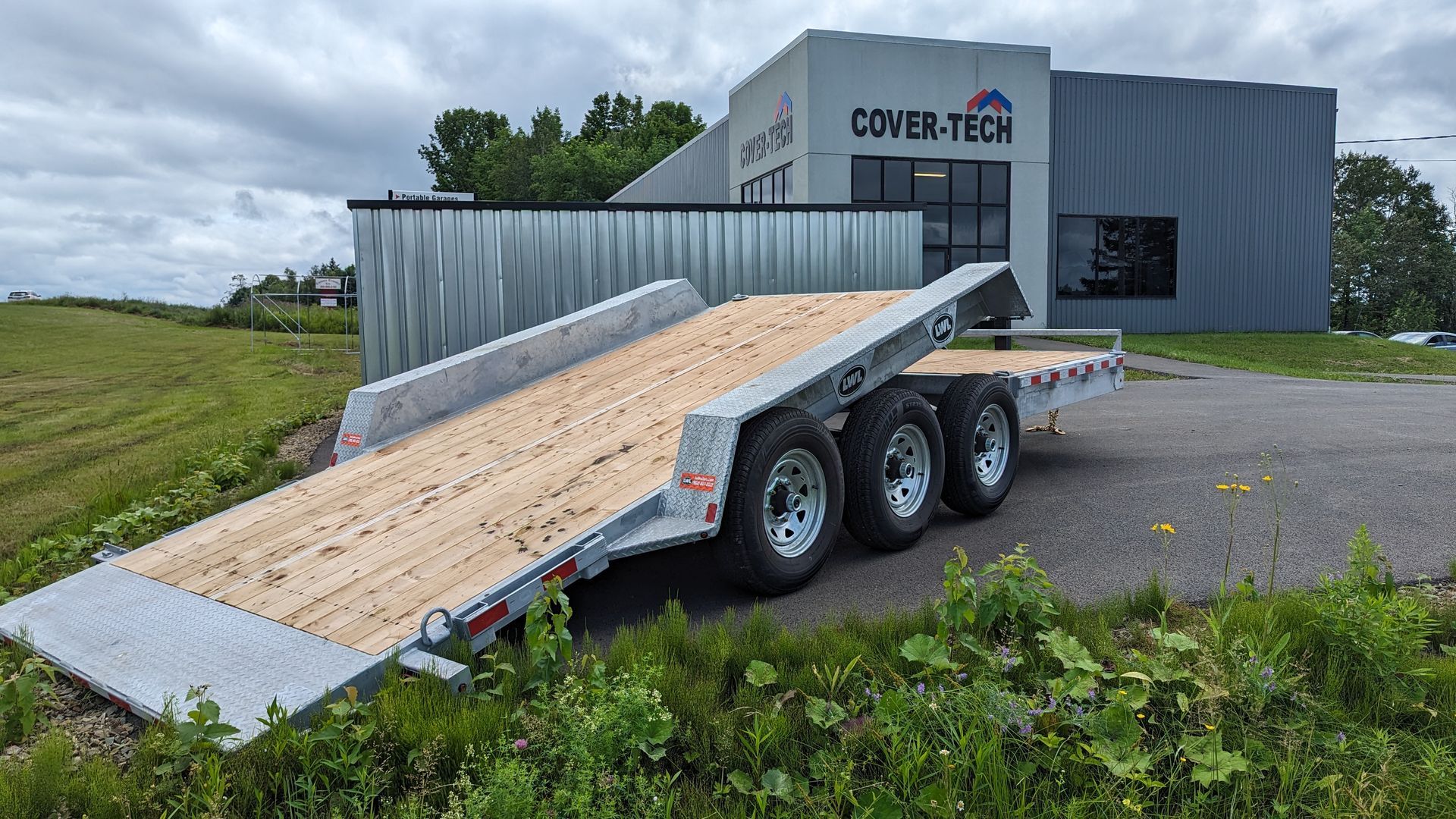 A trailer is parked in a grassy field in front of a building.