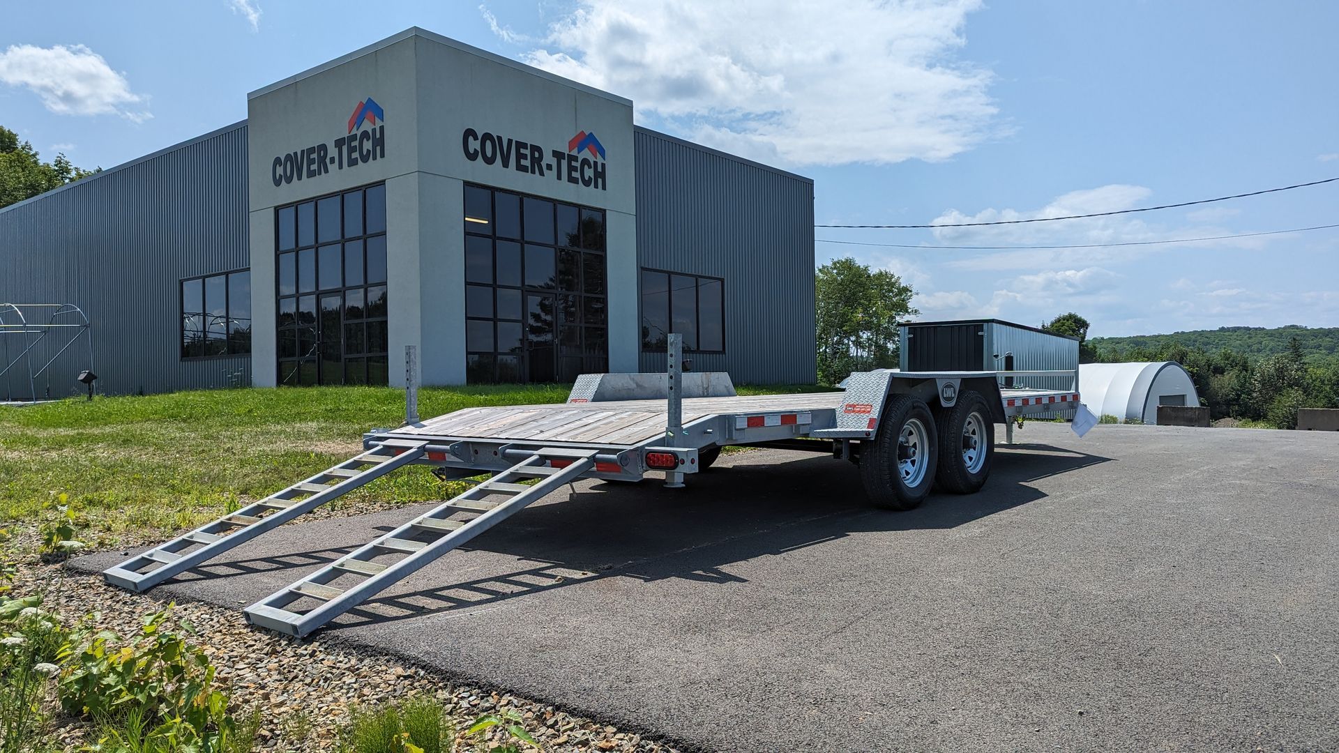 A trailer with ramps is parked in front of a building.