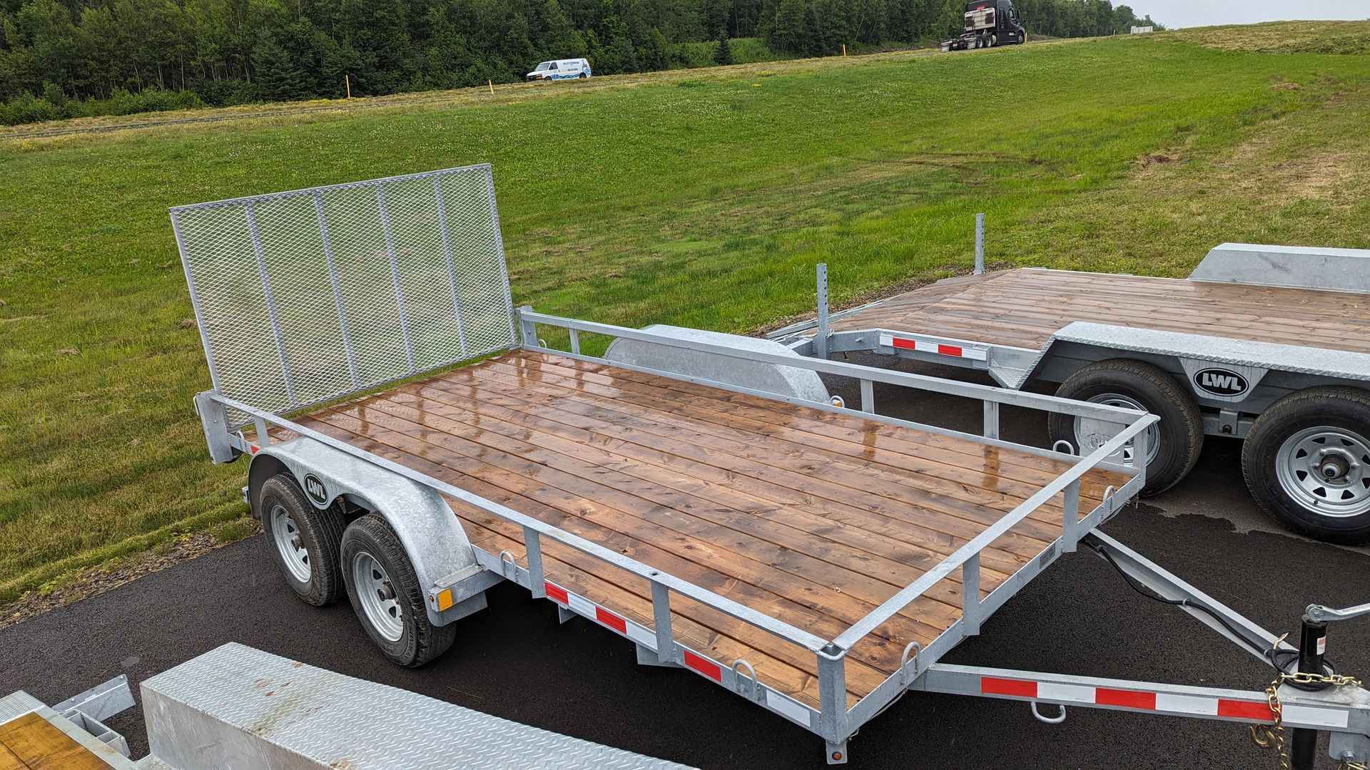 A trailer with a wooden deck is parked on the side of the road.